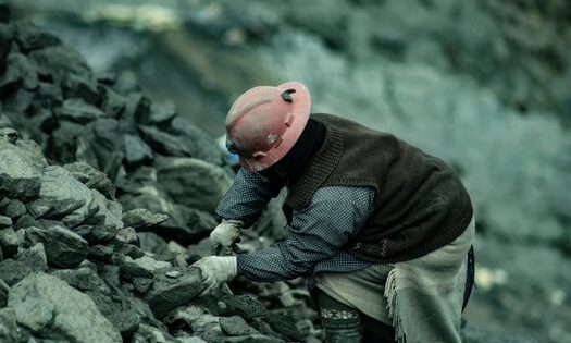 pexels-photo-17839774-17839774 A coal miner in a hard hat working amidst rocky terrain, emphasizing labor and resilience.