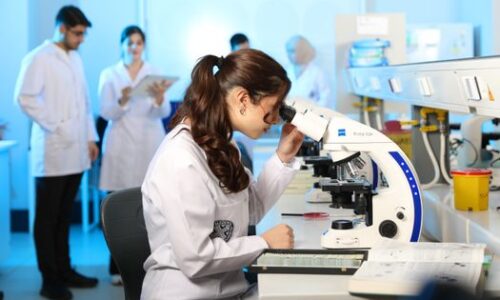 Young female scientist examining samples under a microscope in a modern laboratory setting.