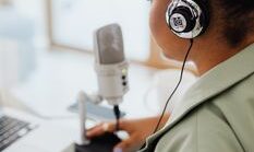 Back view of a woman recording a podcast indoors using a microphone and headphones.