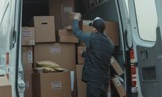 A courier organizing boxes in a delivery van for shipment on a cloudy day.