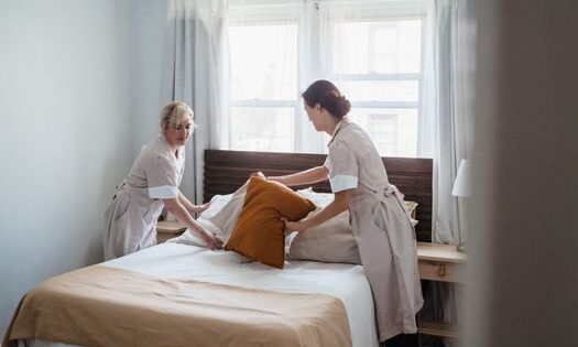 pexels-photo-9462347-9462347 Two housekeepers organizing bed linen in a bright, cozy bedroom.